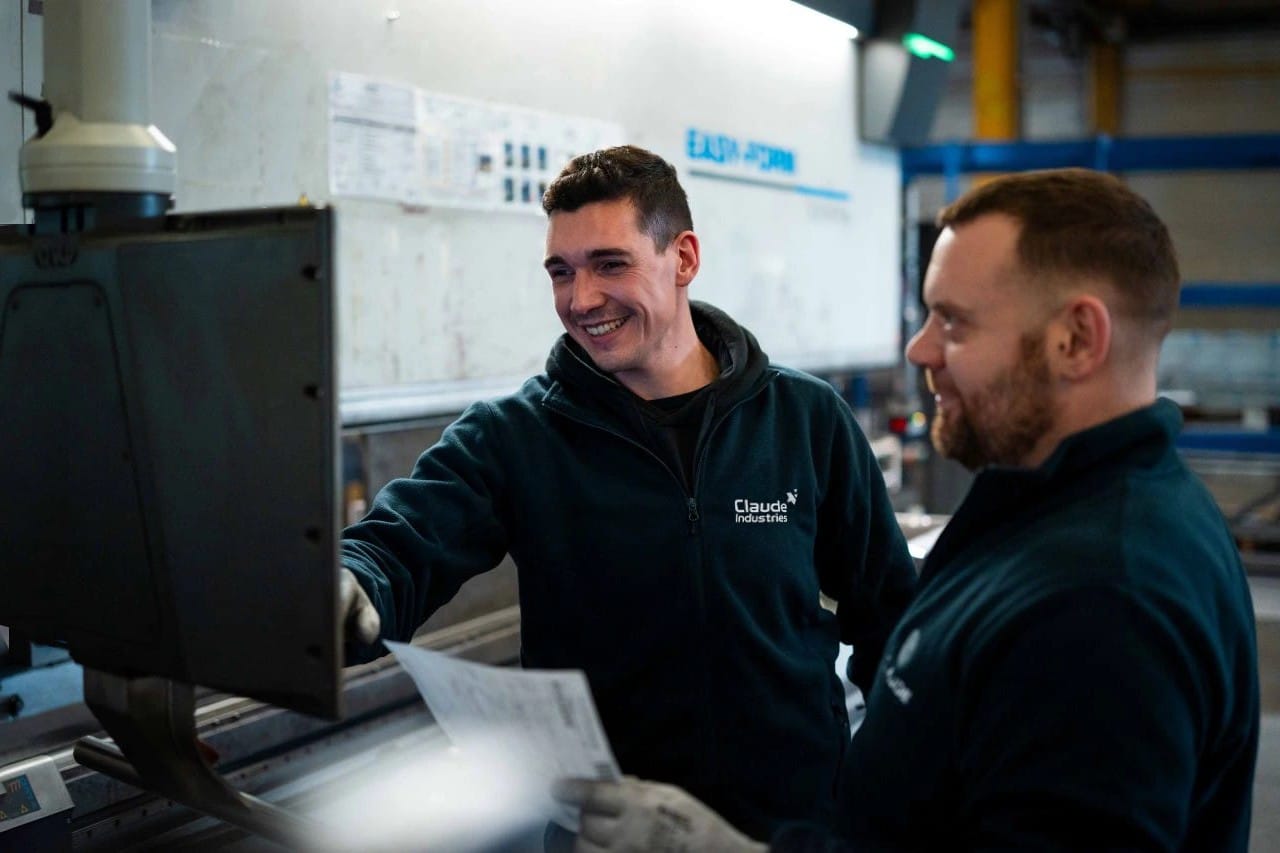 2 régleurs plieurs de Claude Industries souriants devant la commande numérique d'une plieuse